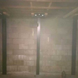 Basement with concrete block walls, dark support beams, and overhead lighting.