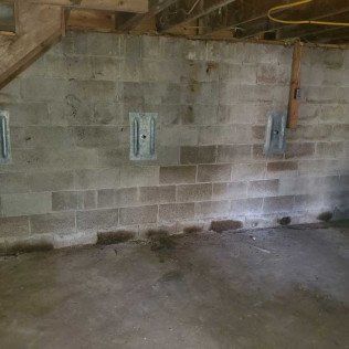 Basement wall with concrete blocks, showing metal plates attached for support.