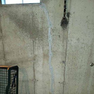 Concrete basement wall with vertical crack sealed with gray caulk; window at top.