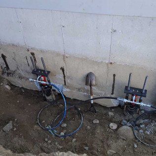 Foundation repair work: hydraulic jacks are used to stabilize a concrete wall; shovel rests nearby.