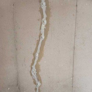A close-up of a wall with a vertical, light-colored sealant line filled in a crack.