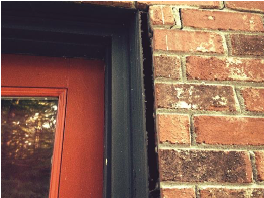 Red door frame next to a brick wall with a black frame.