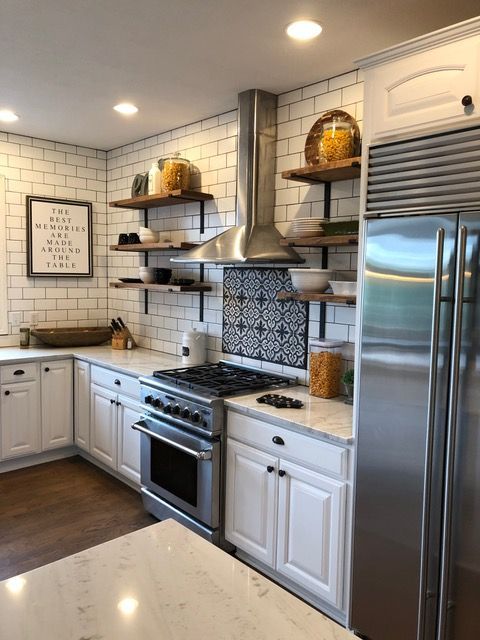 White kitchen with stainless steel appliances, subway tile backsplash, and wooden open shelving.