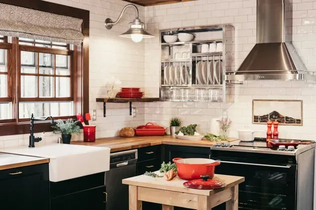 Cozy kitchen with black cabinets, white backsplash, farmhouse sink, and a red Dutch oven on a wooden table.