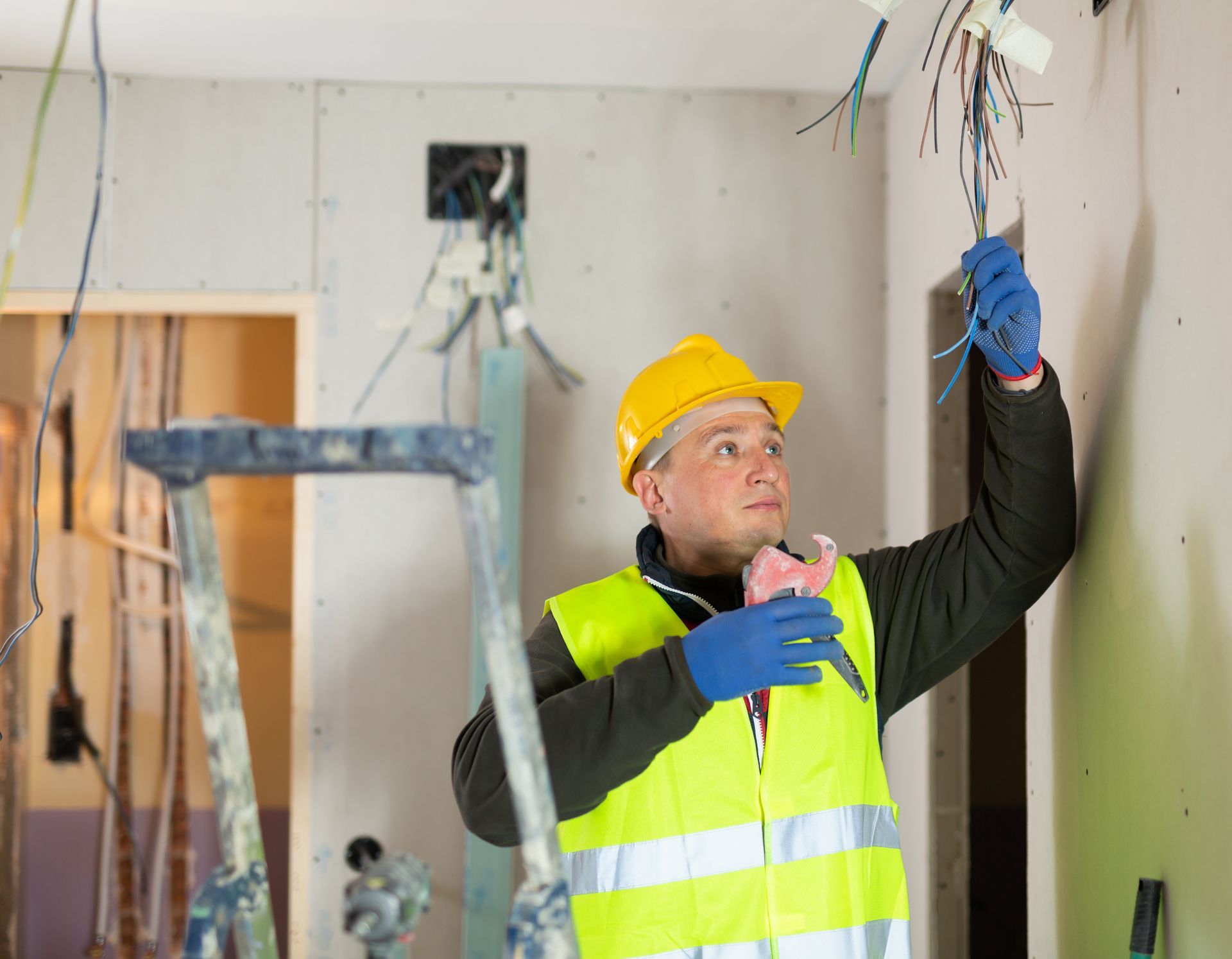 Electrician in a yellow hard hat and vest working on wires inside a building.