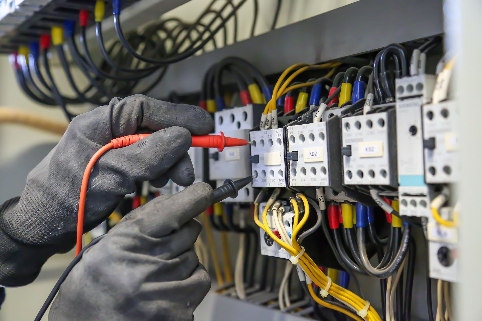 Electrical services technician testing industrial control panel wiring with diagnostic equipment.