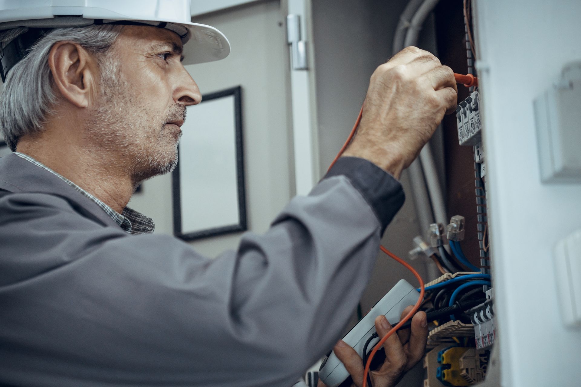 Electrician working on electrical panel with tools and wires, performing maintenance or repair.
