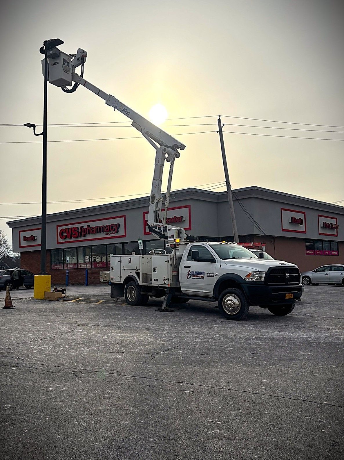 A utility truck with extended boom repairing a sign at a Redner's supermarket on a cloudy day.