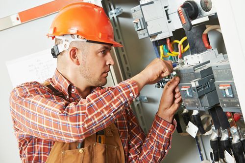 Male electrical engineer with orange cap checks a system of electrical brakers.