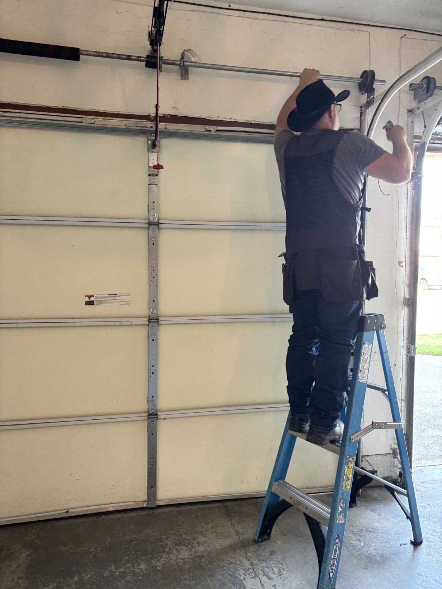 Person on ladder repairing a garage door.