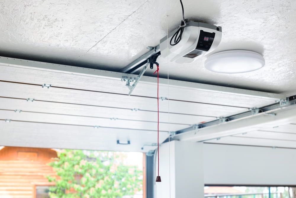 Garage door opener mounted on the ceiling with a pull cord, beside a light fixture.