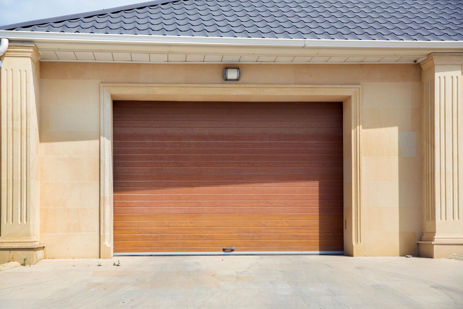 Brown garage door with light tan trim on a light tan building with a gray tiled roof.
