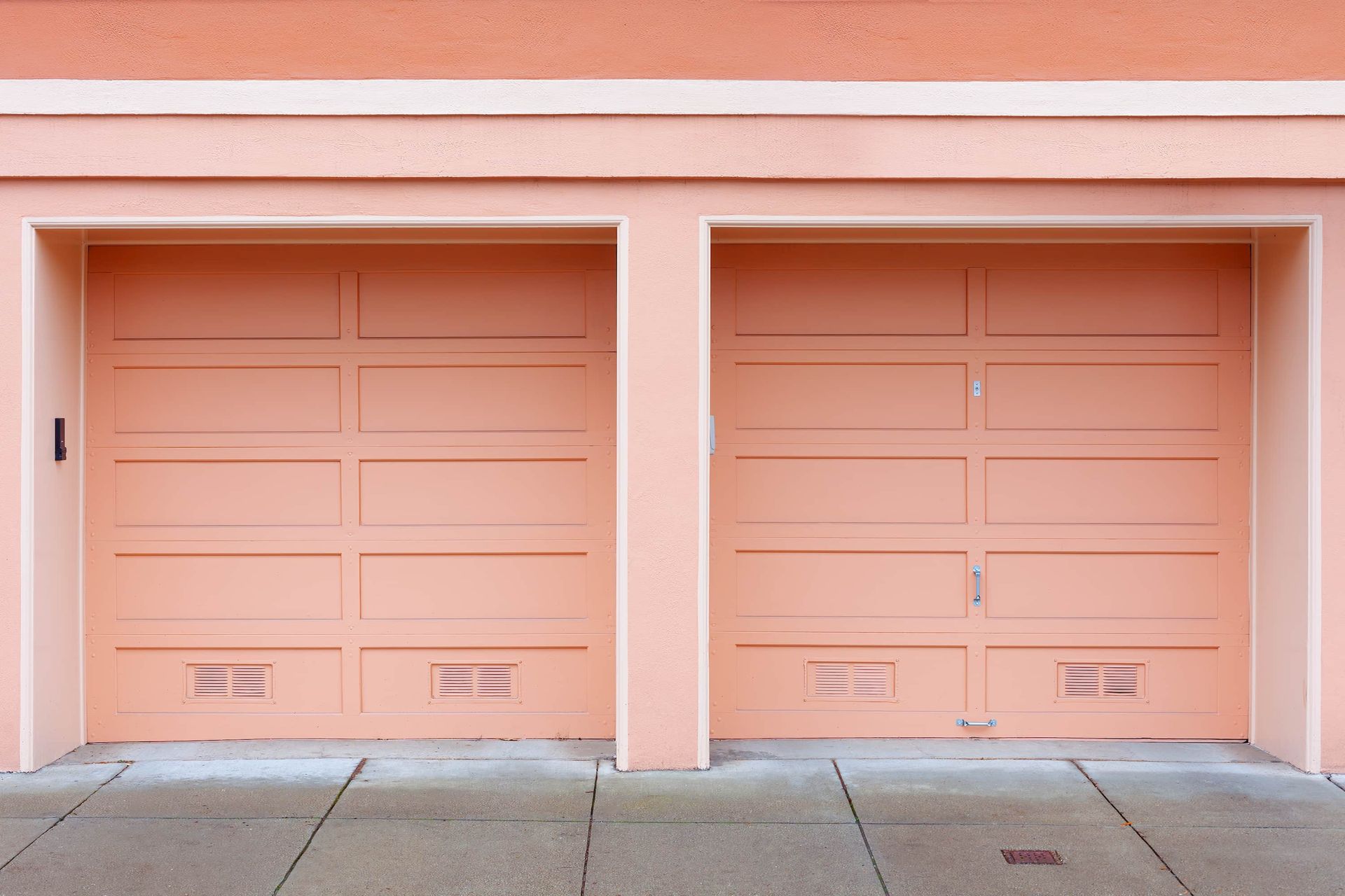 Peach-colored double garage doors on a building with a concrete sidewalk.