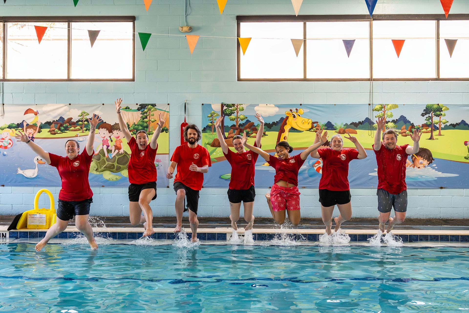 A group of people in red shirts are jumping into a swimming pool.