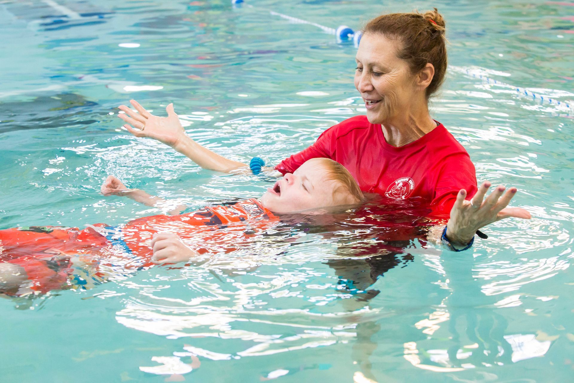 A woman is celebrating a boy as he floats on his back in a swimming pool.