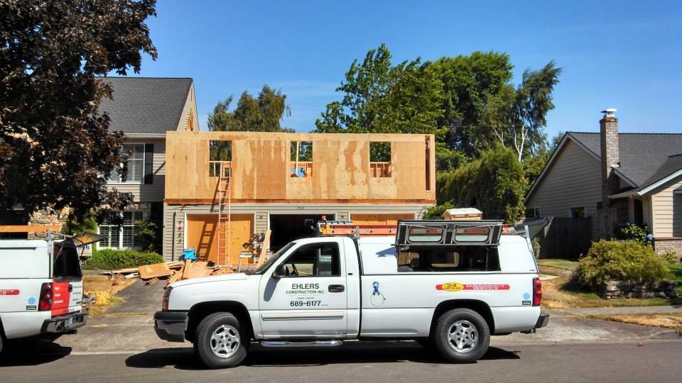 Construction site: Garage with new wooden second story under construction. White work trucks parked in front.