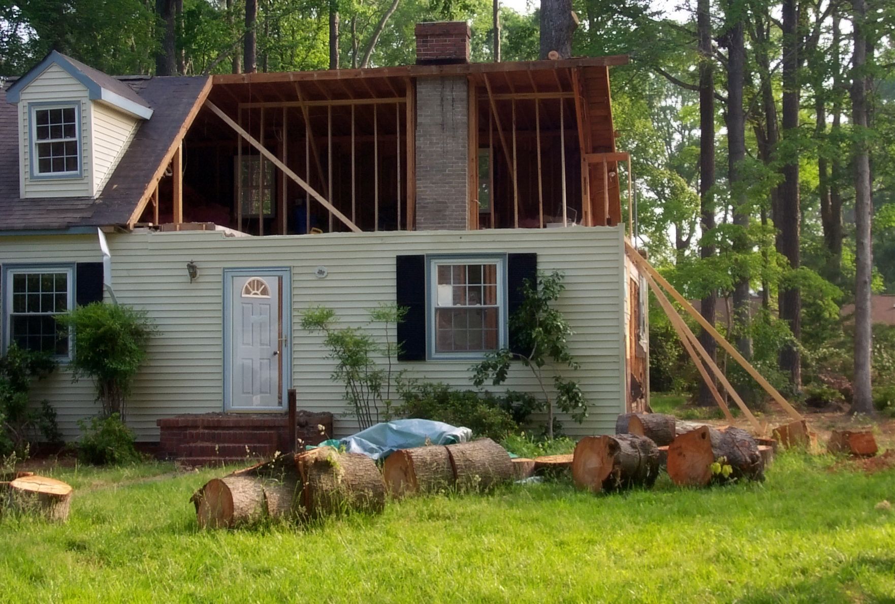 House undergoing renovation, with exposed framing and logs in the yard.