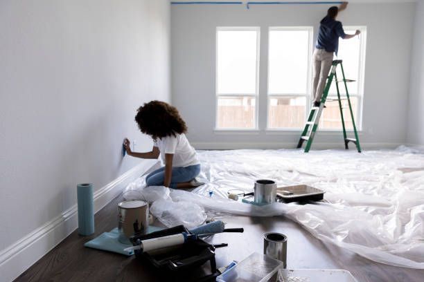 A man and a woman are painting a wall in a room.