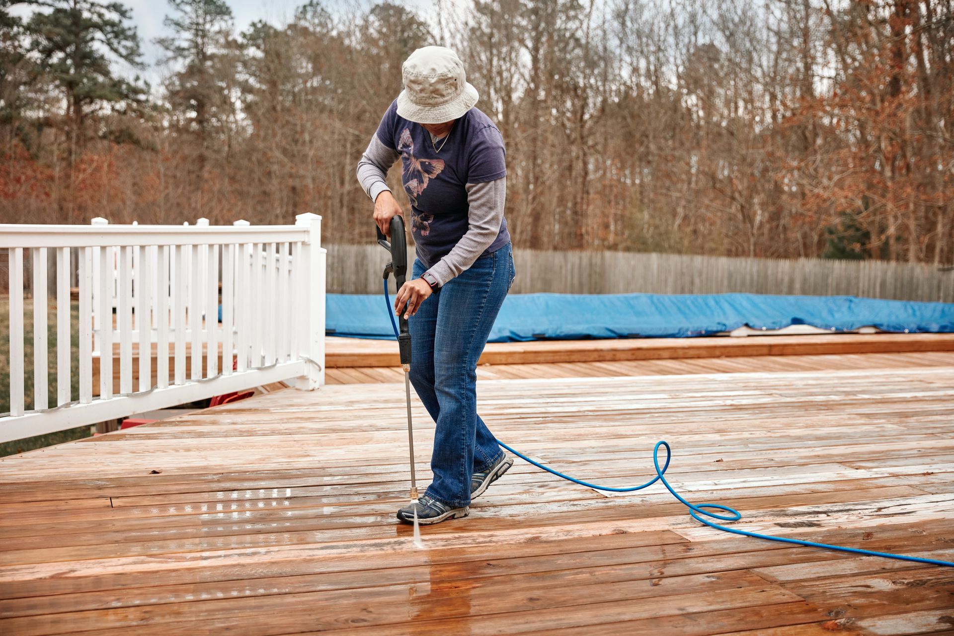 A woman is using a pressure washer to clean a wooden deck.
