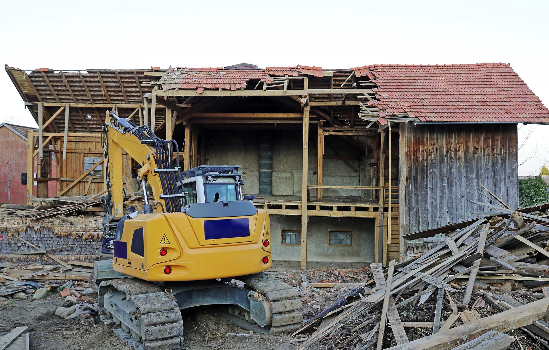 A yellow excavator is demolishing an old wooden house.
