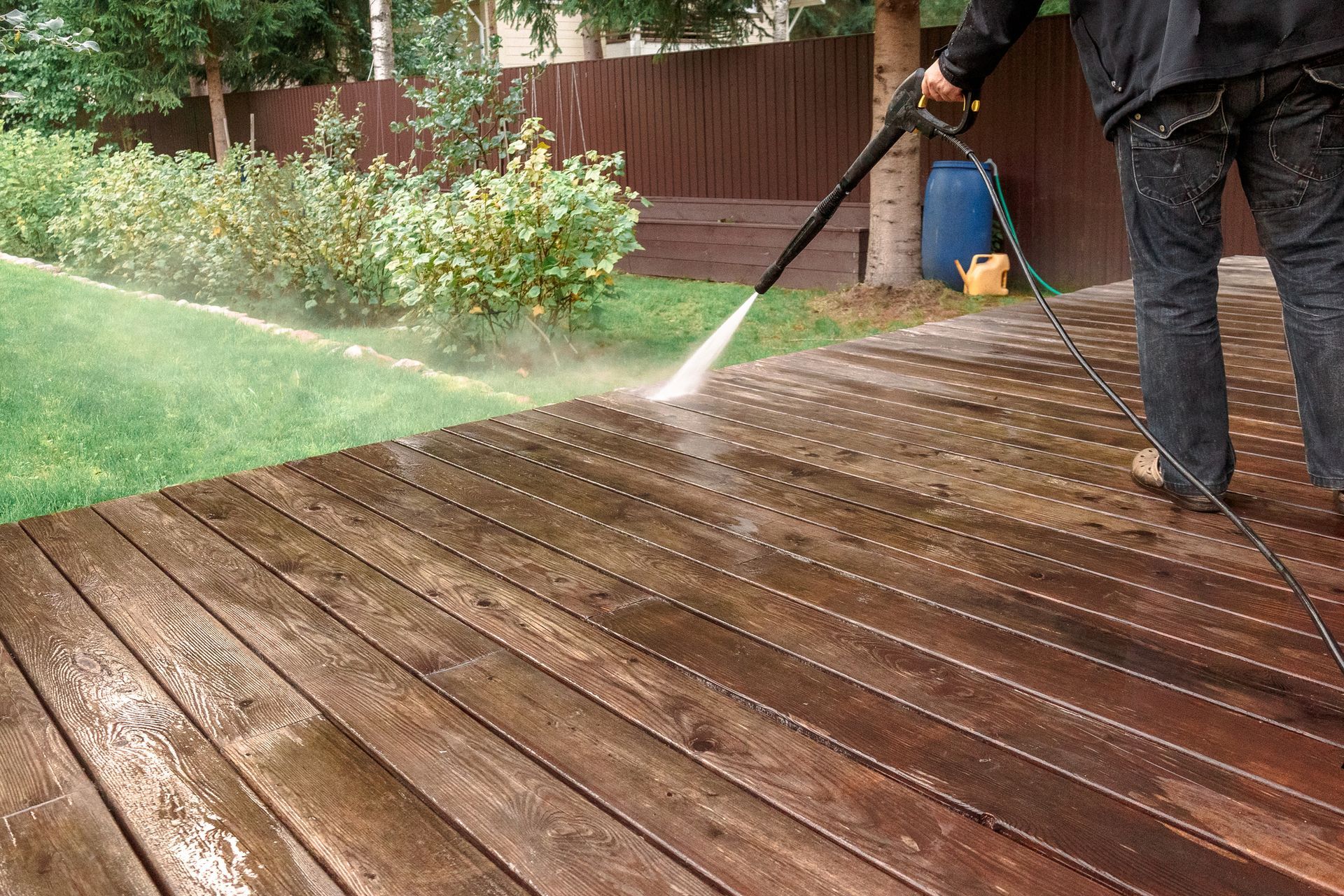 A man is using a high pressure washer to clean a wooden deck.