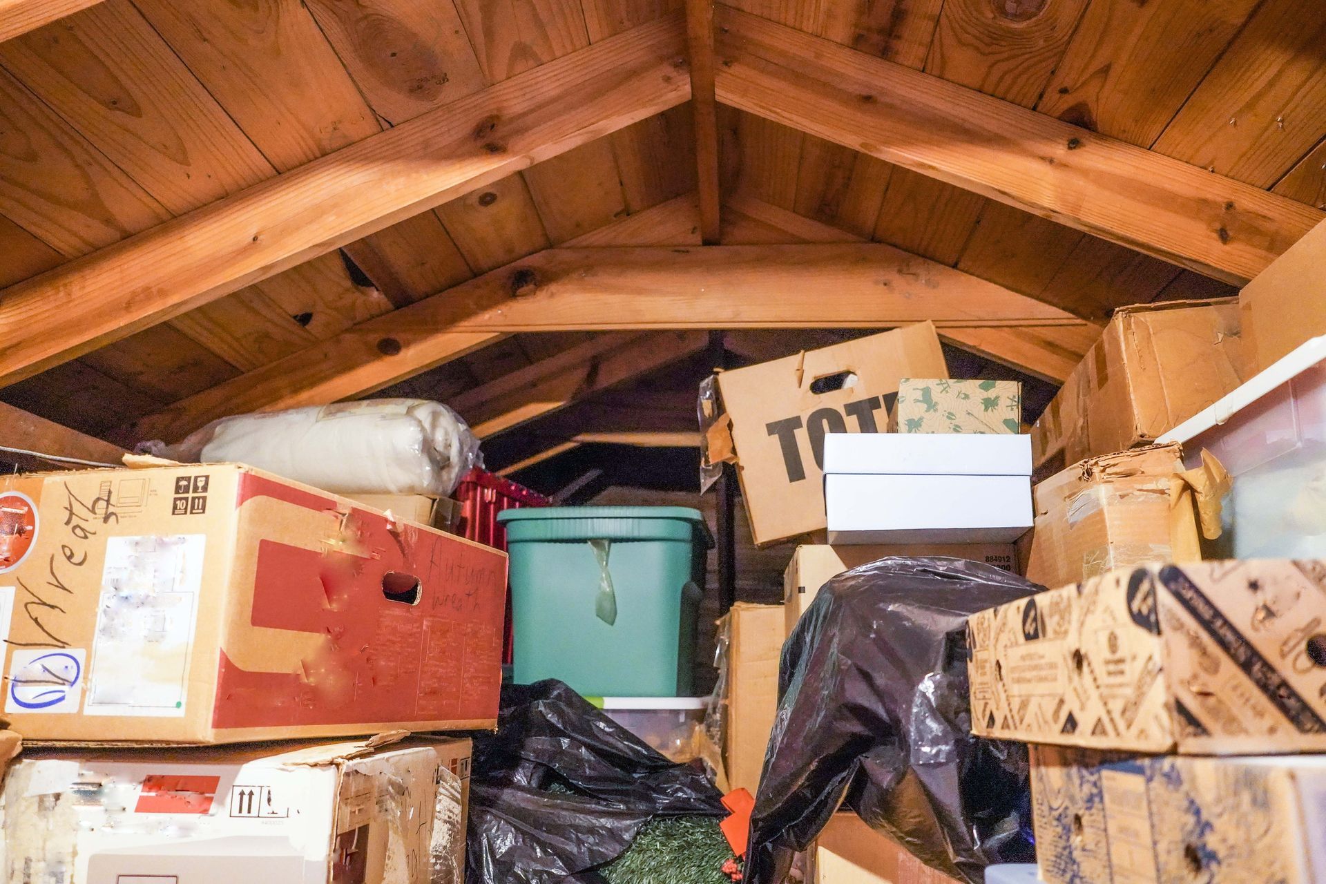 A wooden attic filled with lots of boxes and plastic bags.