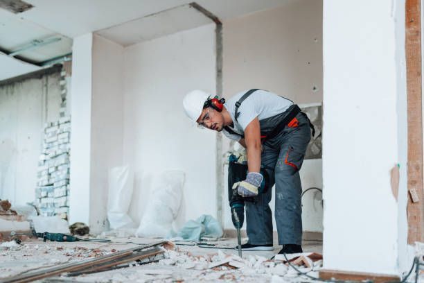 A man is using a hammer to break a wall in a room.