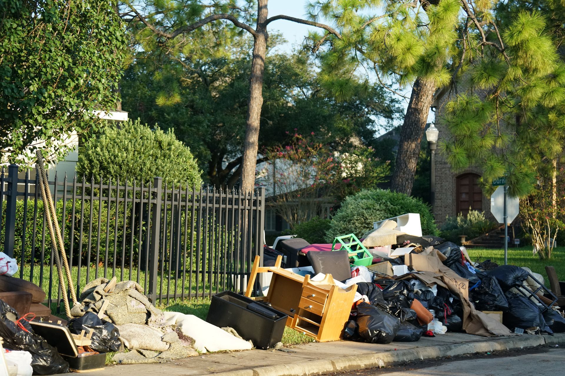 A pile of trash is on the side of the road in front of a house.