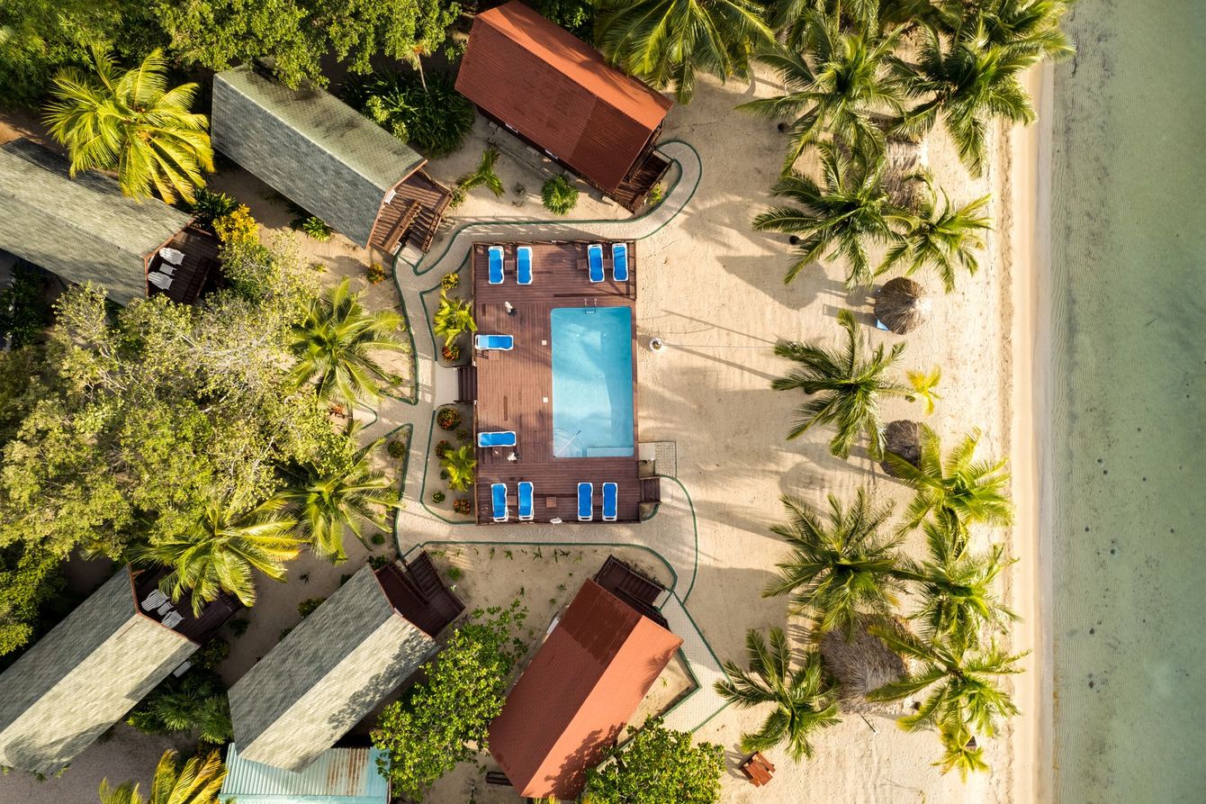 An aerial view of a beach resort with a swimming pool surrounded by palm trees.