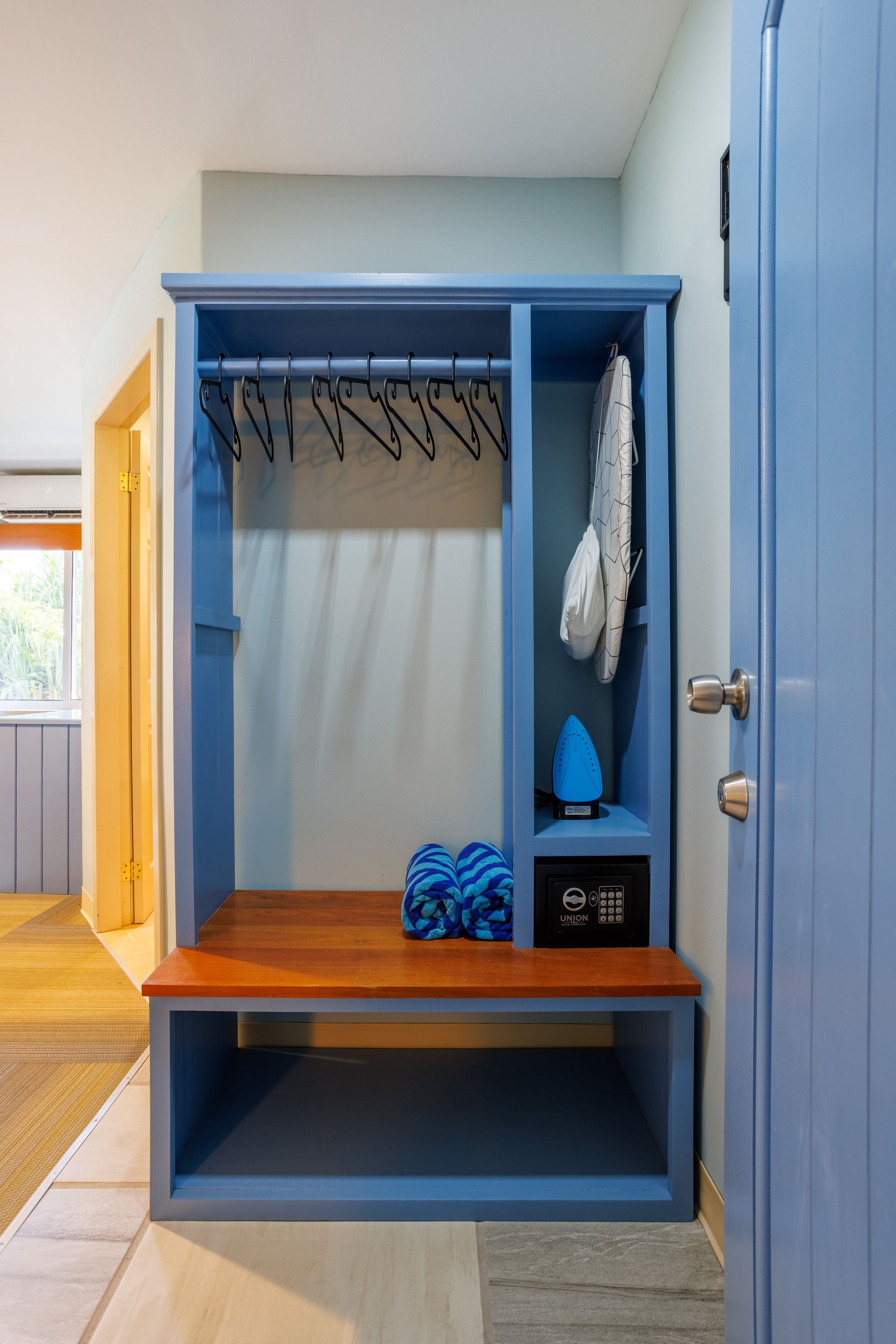 A blue closet with a wooden bench in a hallway.