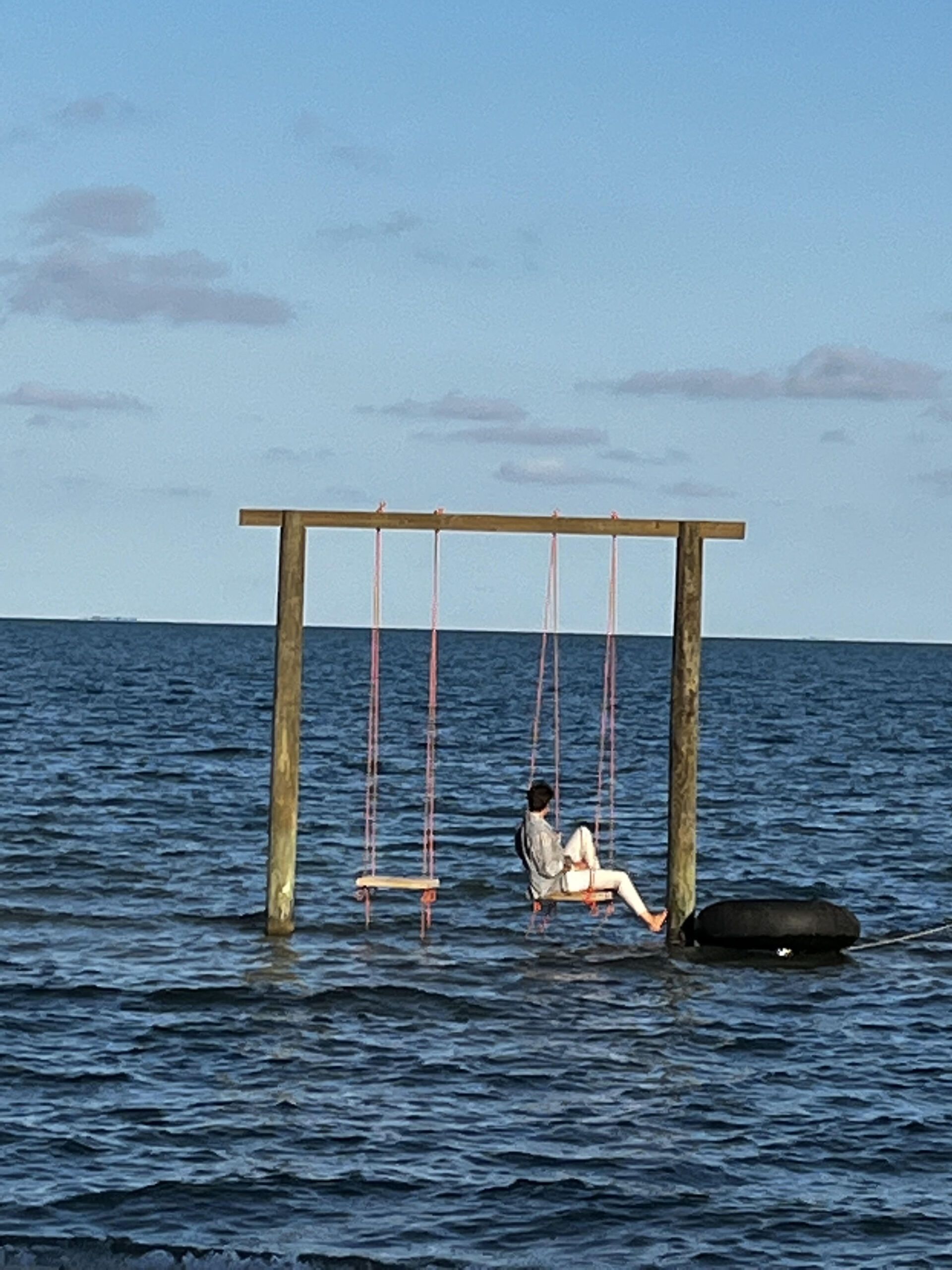 A woman sits on a swing in the middle of the ocean
