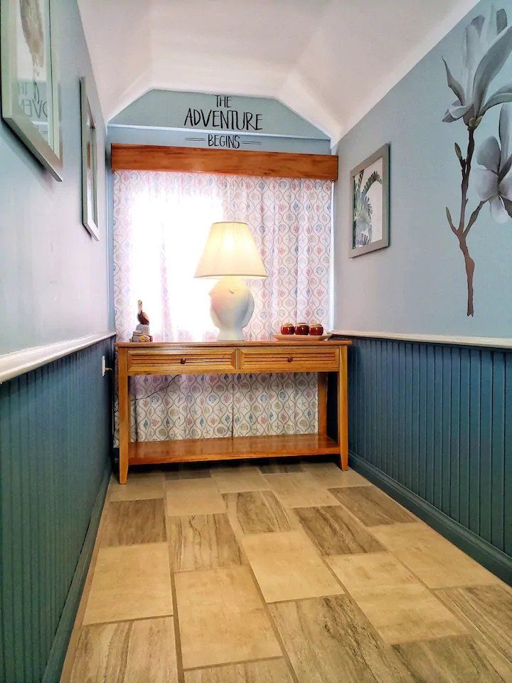 A hallway with a table and a lamp and the word adventure on the wall