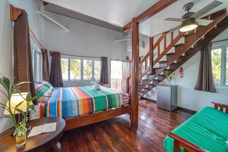 A bedroom with a bed , table , stairs and a ceiling fan.