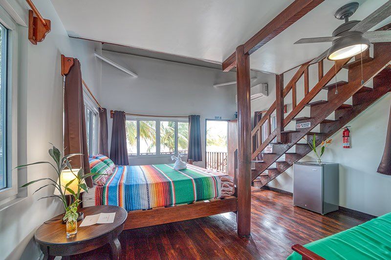 A bedroom with a bed , stairs , a table and a ceiling fan.
