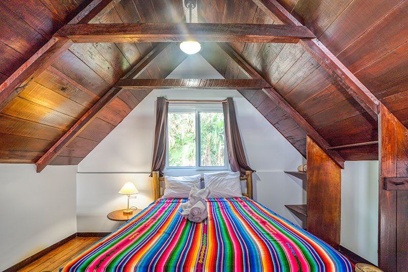 There is a bed with a colorful blanket in the attic.