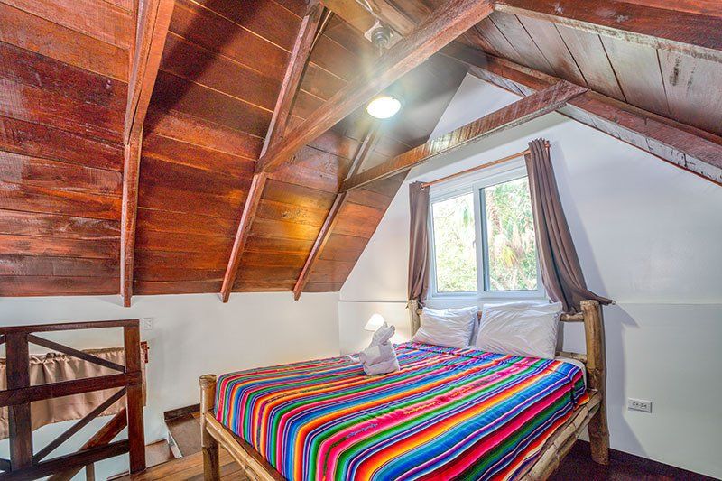 A bed with a colorful blanket in a bedroom with a wooden ceiling.
