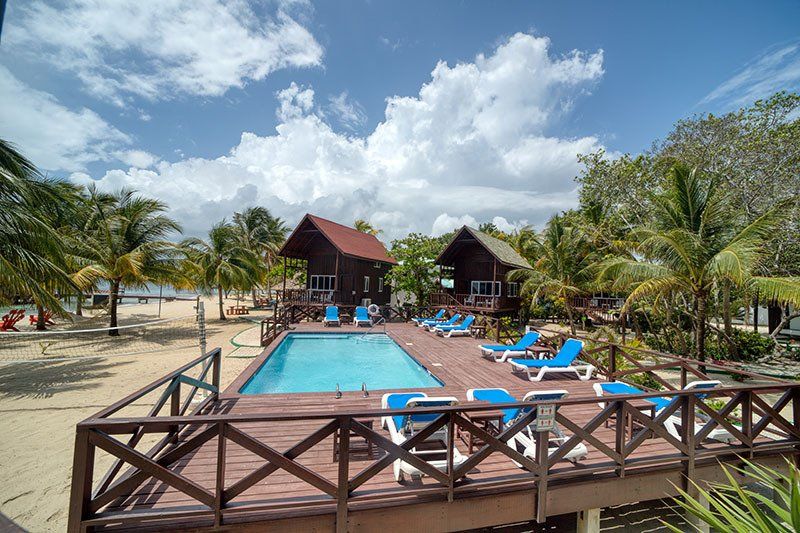 A swimming pool surrounded by chairs and a wooden deck on a beach.
