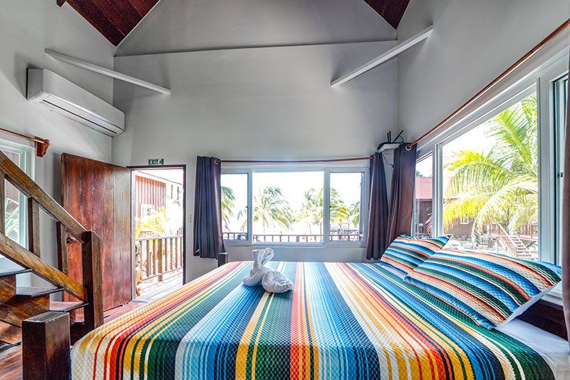 A bedroom with a king size bed , stairs , and a large window.