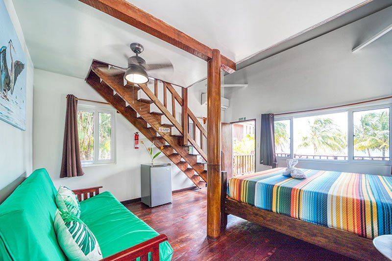 A bedroom with a couch , bed , stairs and a ceiling fan.