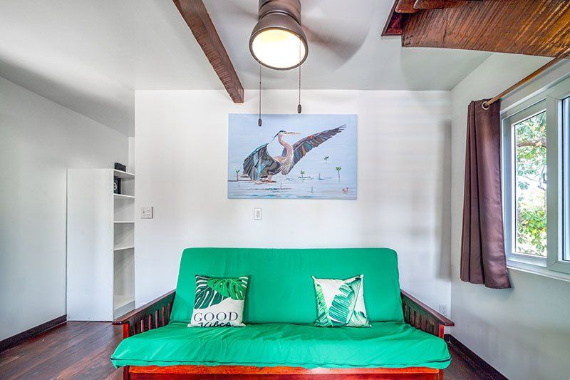 A living room with a green futon and a painting on the wall.
