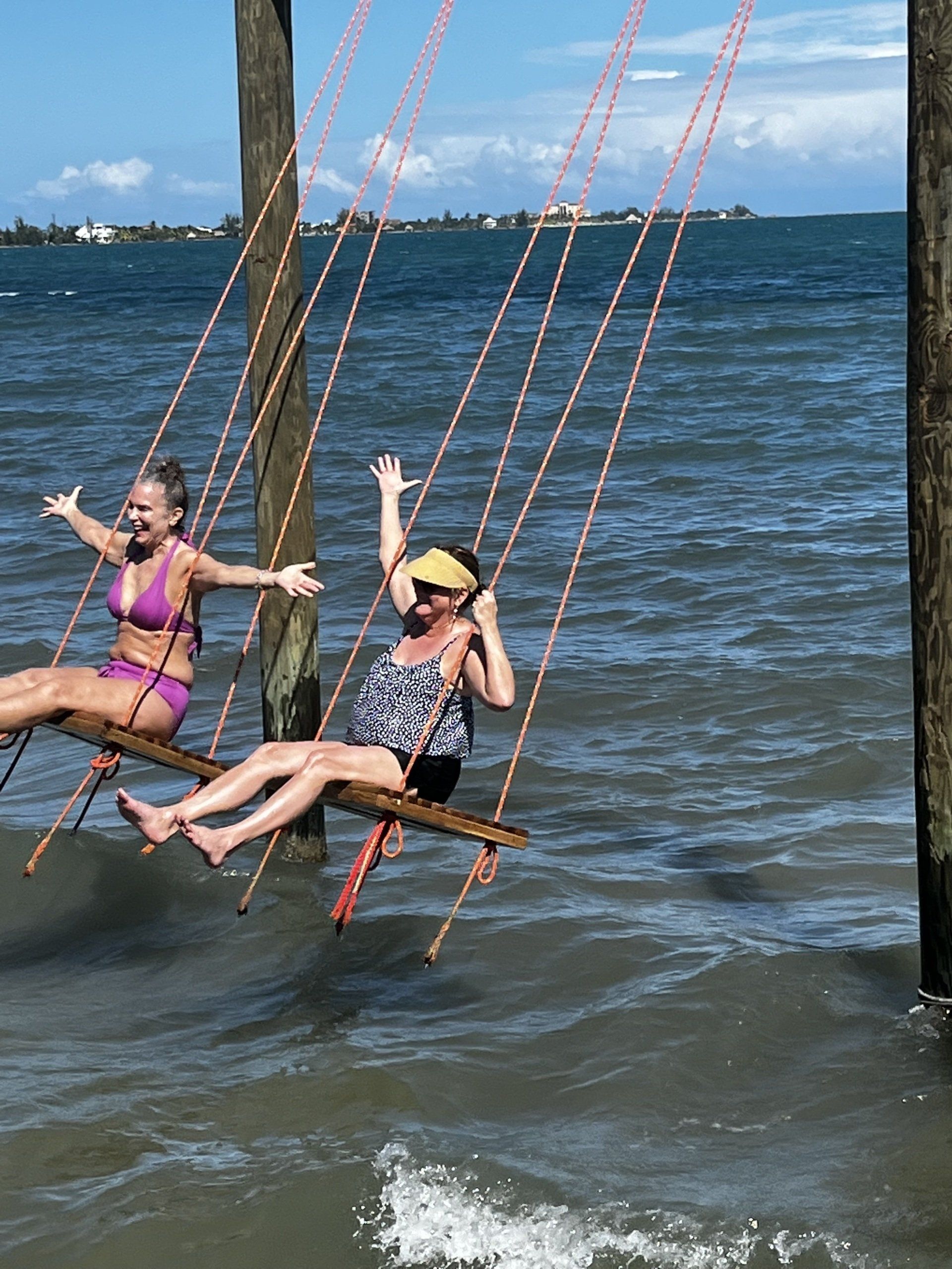 Two women are sitting on swings in the water