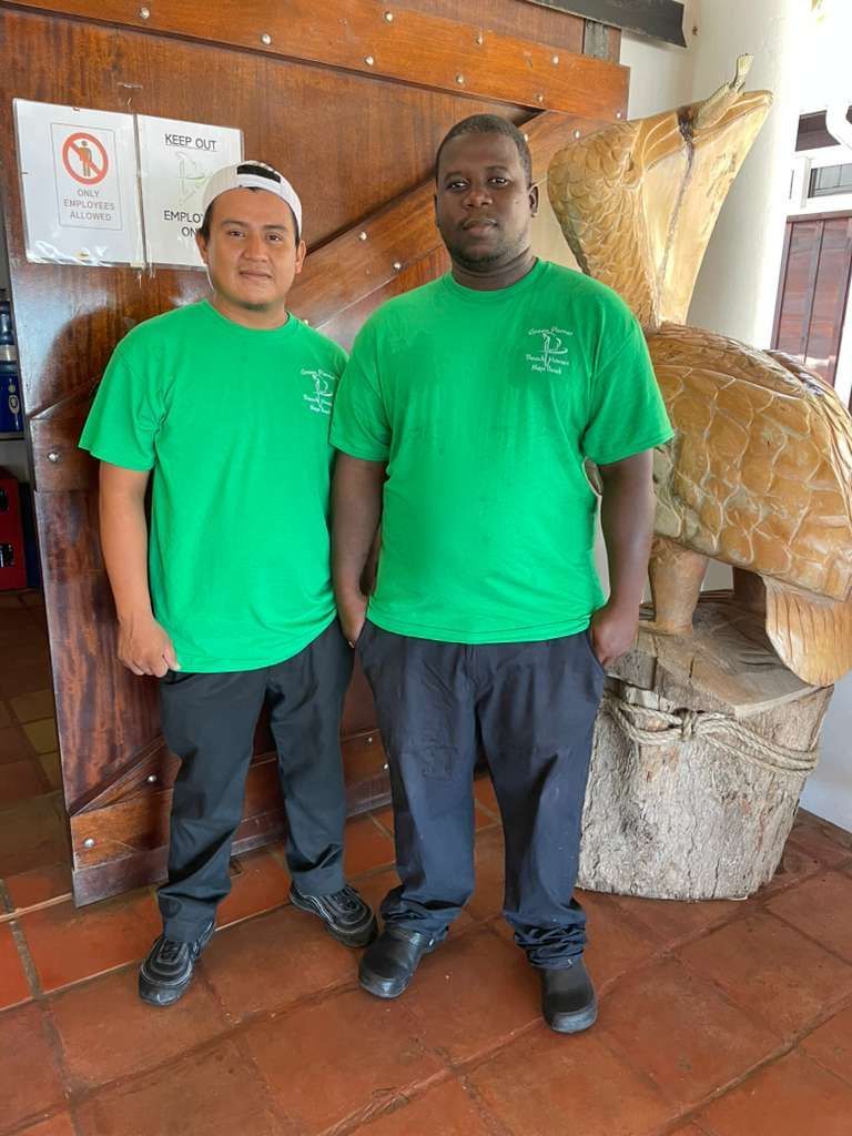 A man in an apron is standing in a kitchen with pots and pans hanging from the ceiling