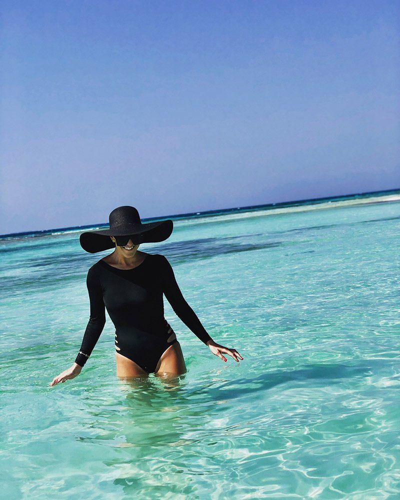 A woman in a black swimsuit and hat is standing in the ocean.