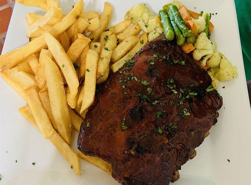 A white plate topped with ribs french fries and vegetables