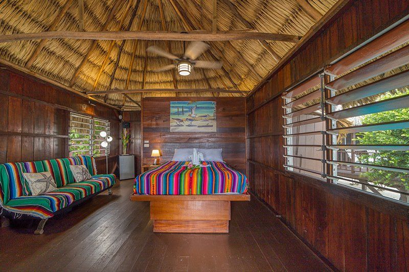 There is a bed in the middle of the room with a thatched roof.