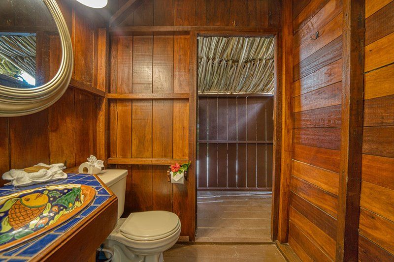 A bathroom with a toilet , sink , mirror and wooden walls.