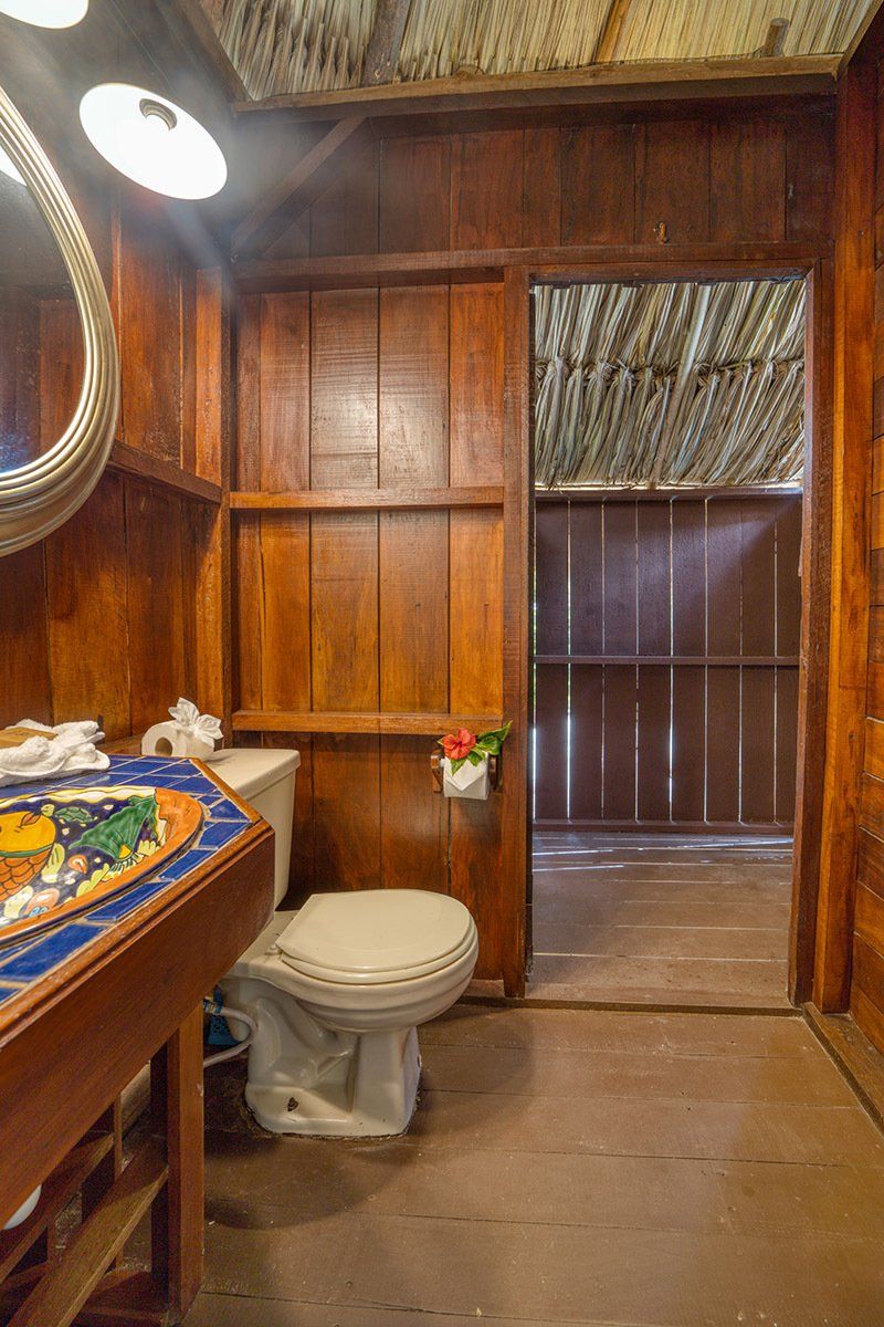 A bathroom with a toilet , sink , mirror and wooden walls.