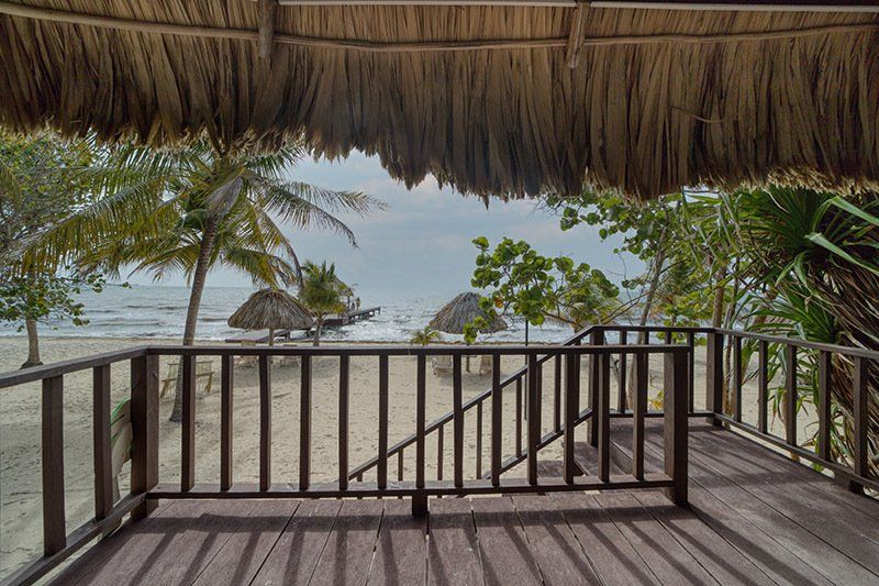 A view of the beach from a balcony with a thatched roof.