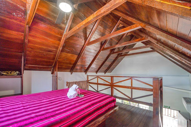 A bedroom with a wooden ceiling and a bed with a pink blanket.