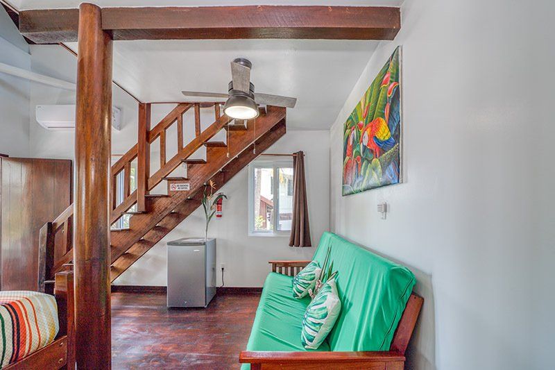 A living room with a green futon , stairs and a ceiling fan.